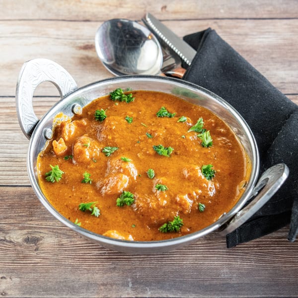 African chicken curry in a metal bowl, garnished with parsley, on a wooden table.