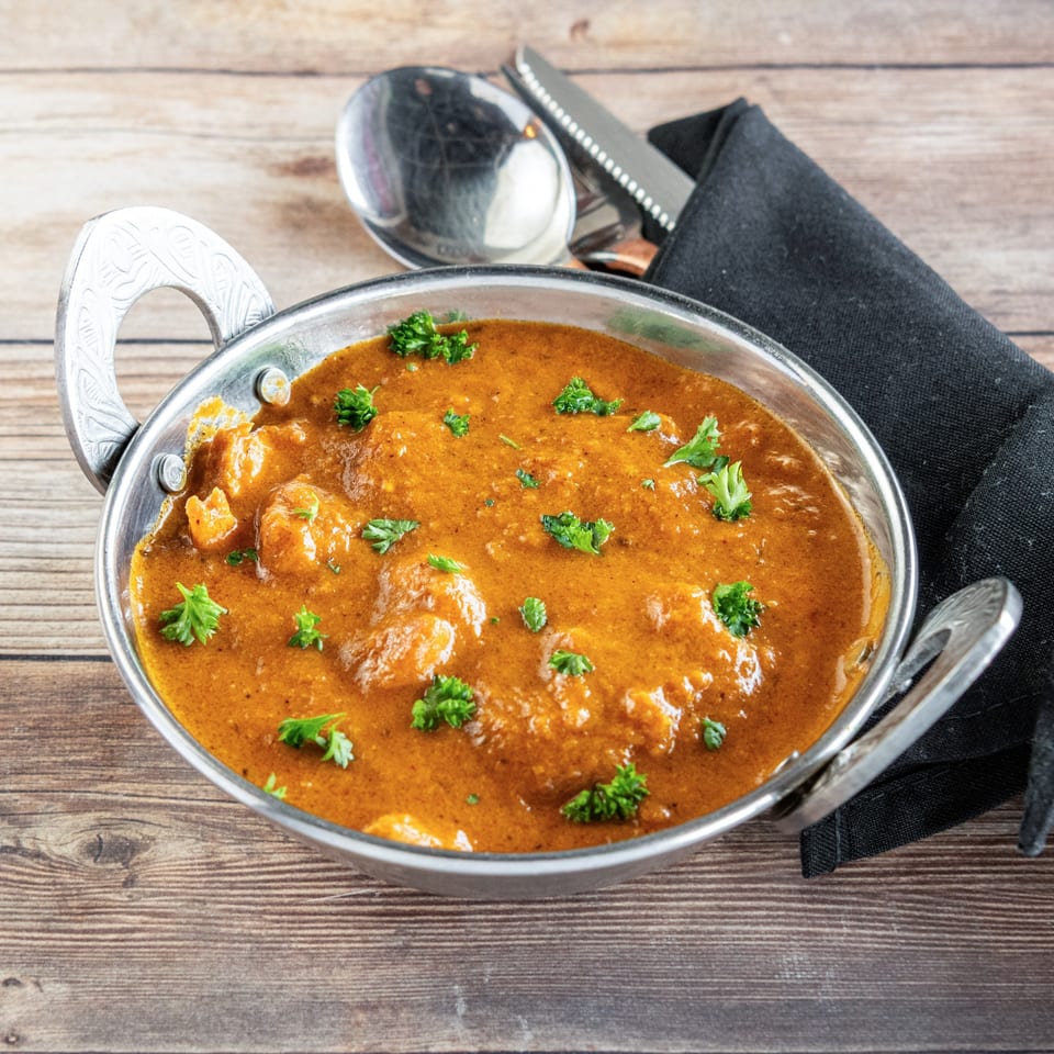 African chicken curry in a metal bowl, garnished with parsley, on a wooden table.