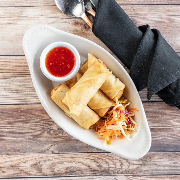 Crispy spring rolls with sweet chili dipping sauce and shredded vegetables on a white plate.
