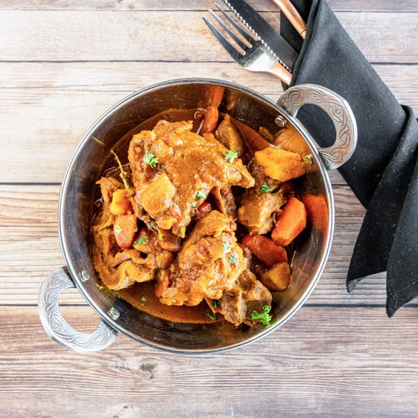 African stew with meat and vegetables in a metal bowl, with cutlery and a napkin.