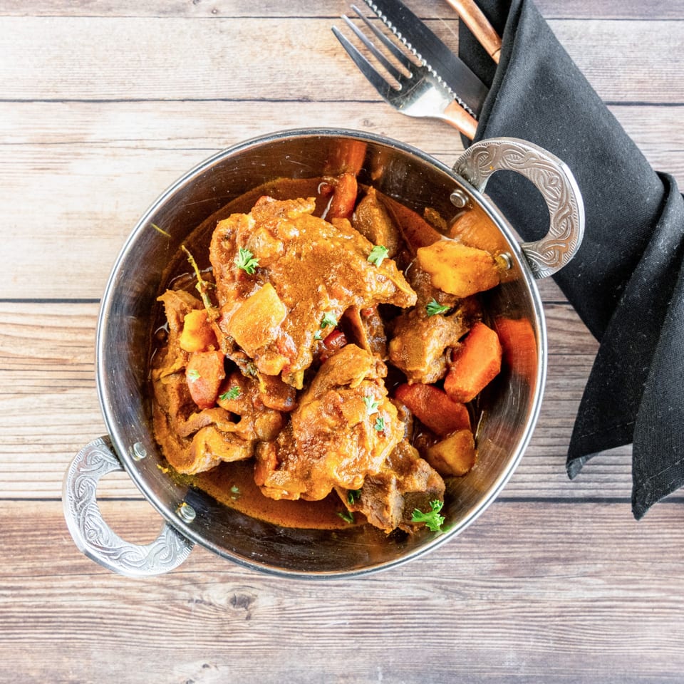 African stew with meat and vegetables in a metal bowl, with cutlery and a napkin.