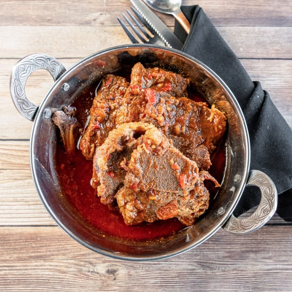African stew with meat and red sauce in a metal bowl on a wooden table with cutlery.