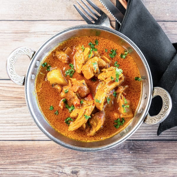 African chicken curry with potatoes and cilantro in a silver bowl on a wooden table.