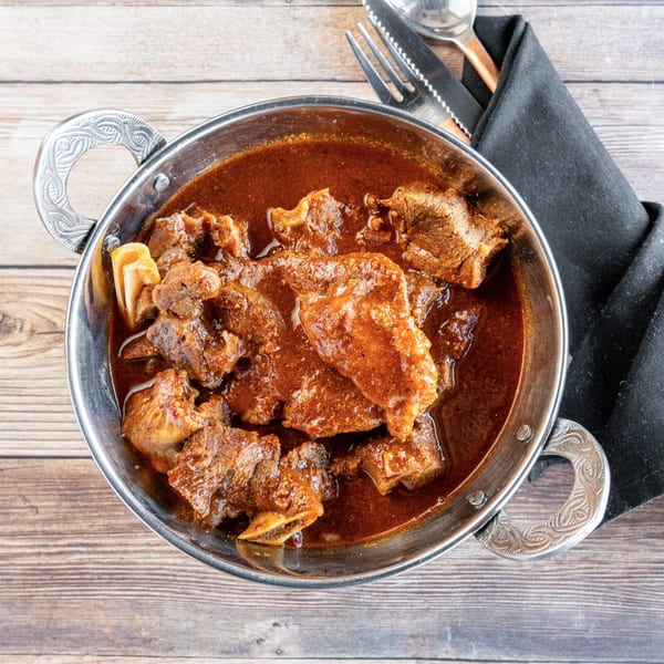 African goat stew, a rich red-brown dish with tender meat pieces, served in a silver bowl.