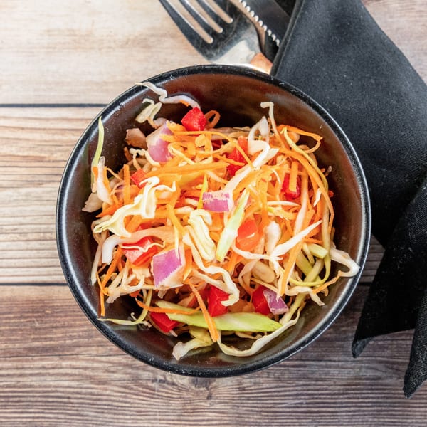 A vibrant African coleslaw with shredded cabbage, carrots, red peppers, and red onions in a black bowl.