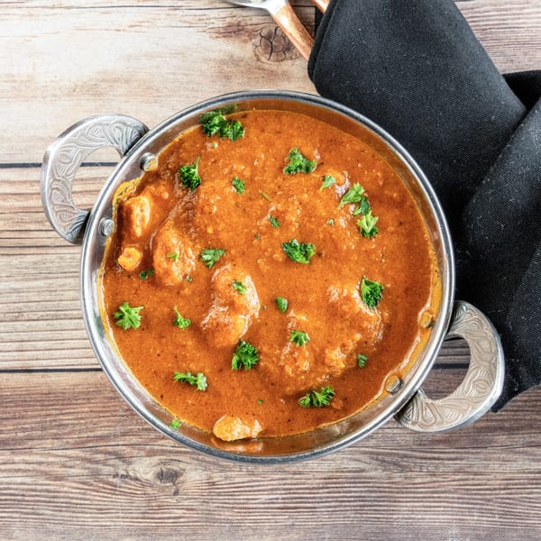 Overhead view of an African curry dish with chicken and parsley in a silver bowl on a wooden table.