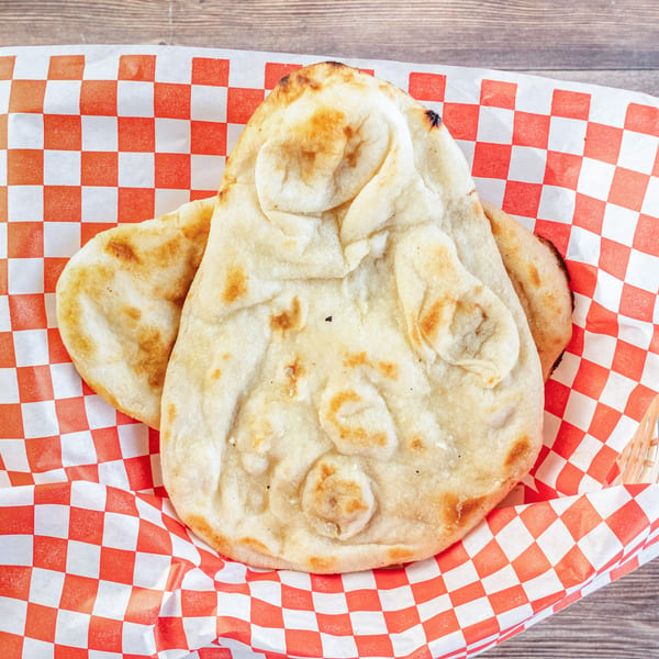 Freshly baked naan bread with golden-brown spots, served in a basket lined with red and white checkered paper.