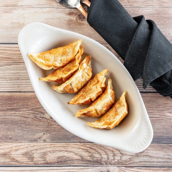 Golden-brown fried dumplings, sprinkled with seasoning, served on a white platter with a black napkin.
